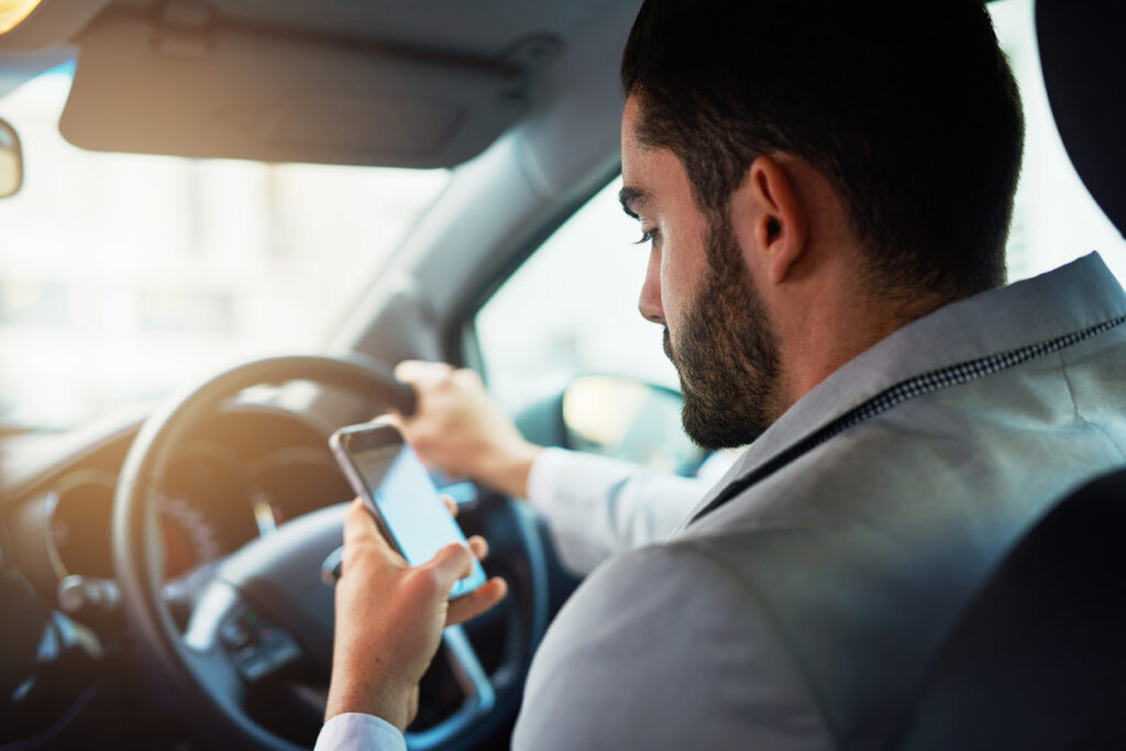¿Cuáles Son Los Peligros De La Conducción Distraída? 22 Un Conductor Masculino Distraído Sosteniendo Un Teléfono Inteligente Mientras Conduce.