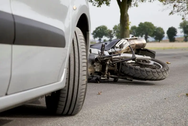 Primer Plano Del Neumático De Un Automóvil Plateado Junto A Una Motocicleta Accidentada Y Tirada En La Carretera.