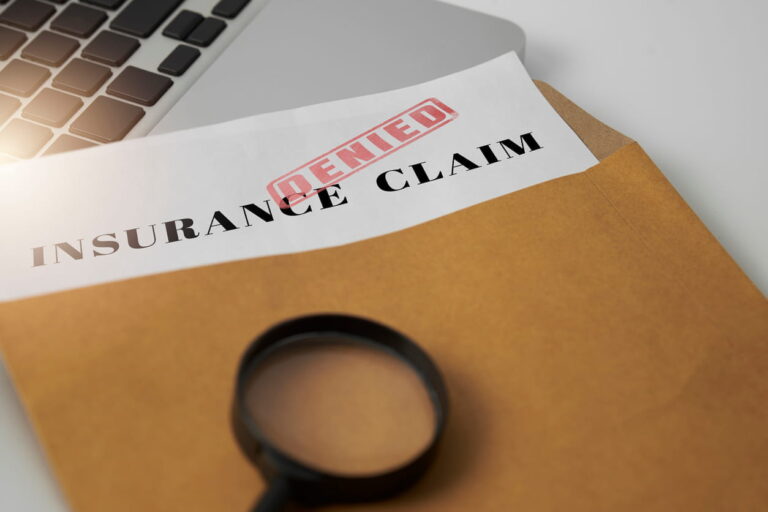 A piece of paper sticking out of a manila envelope that reads "Insurance Claim Denied."