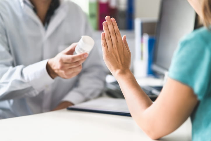 A woman is holding her hand up, refusing medication from a doctor.