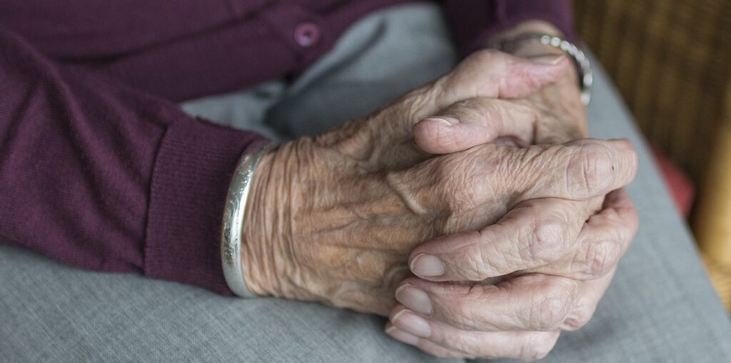 A closeup image of an elderly person with their hands clasped together.