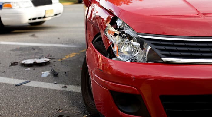 An upclose view of a damaged front end of a red vehicle after it's been in a car accident.