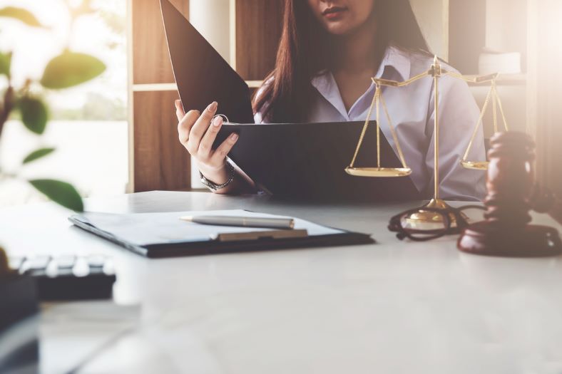 A female car accident attorney reviewing a case at her desk. On her desk is paperwork, the scales of justice, and a gavel.