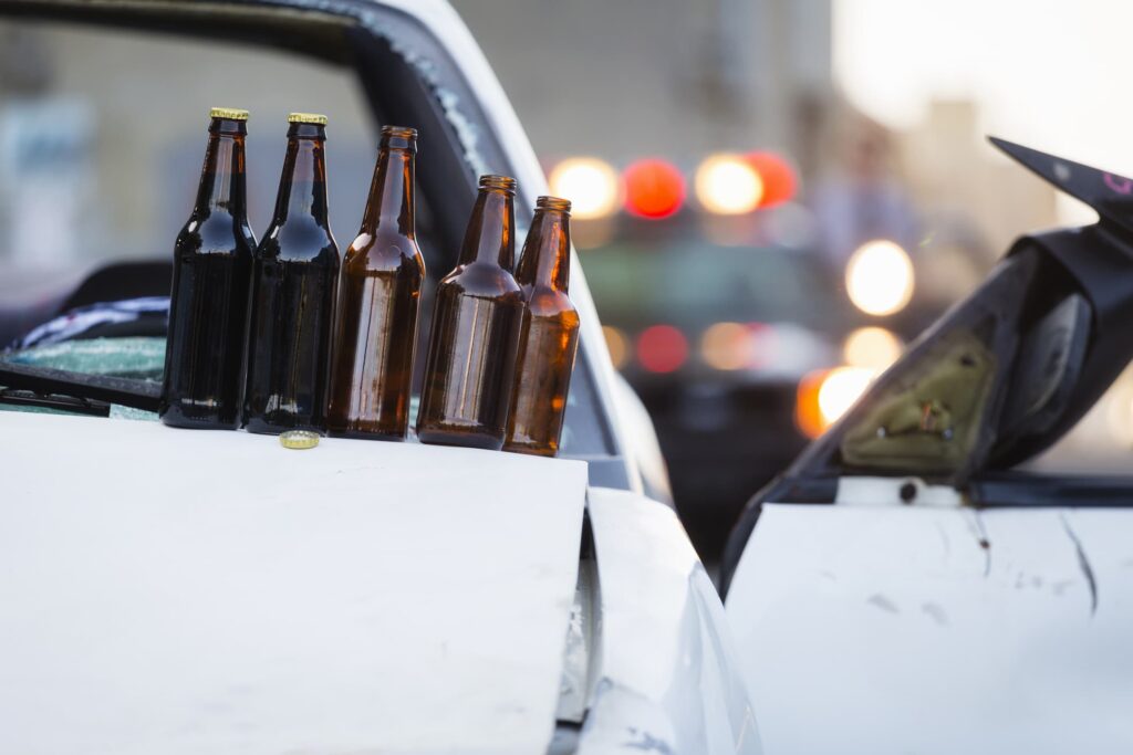 3 of 5 beer bottles are empty as they sit on the hood of a vehicle after drunk driving.