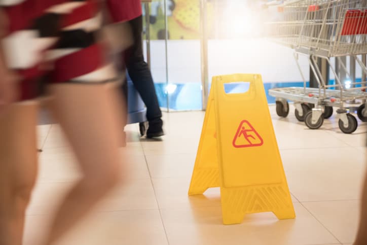 A yellow caution sign warns people of a slip-and-fall risk inside a store.