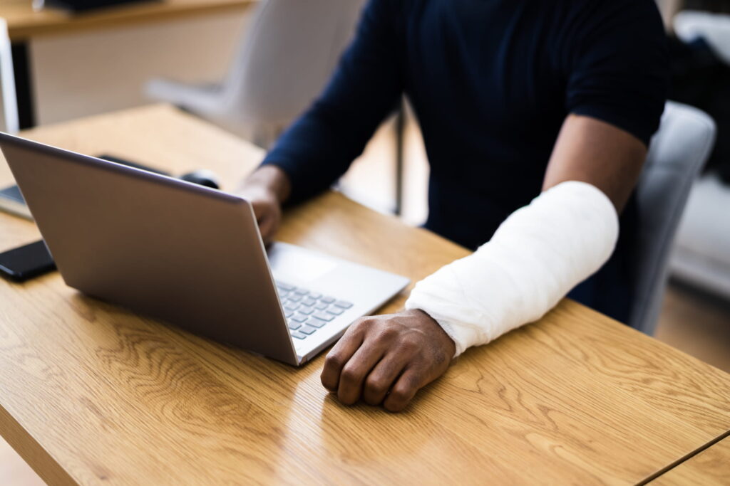 man on workers compensation with injured hand working on a laptop