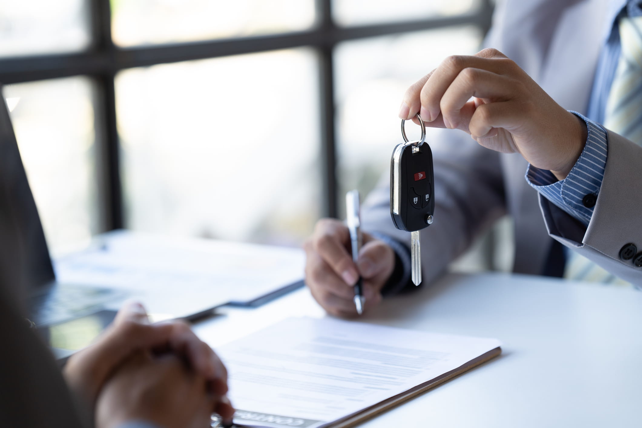 auto insurance agent handing keys to client as they sign documents