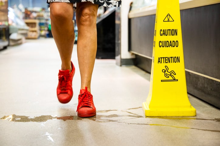 A person walks through a puddle on the floor next to a caution sign, which is a risk to a slip-and-fall accident.