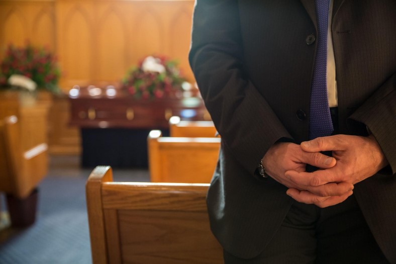 man holding his hands together at a funeral inside a church