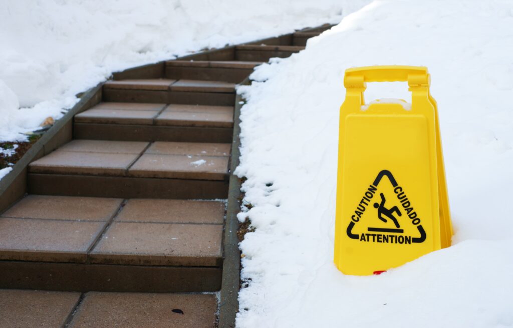 yellow caution sign outside in snow by walkway