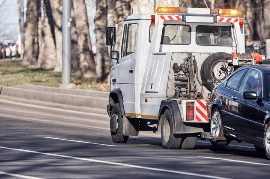a white tow truck towing a black vehicle after it's been in a motor vehicle accident