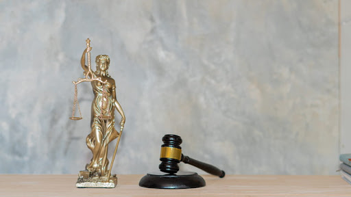 A statue holding the scales of justice in one hand and a sword in the other. Next to the statue is a gavel.