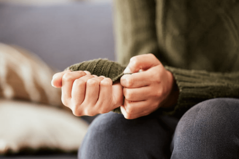 focus is on the hands of a distressed woman clutching her sweater.