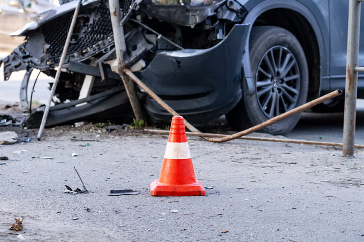 An up-close view of a severely damaged vehicle after a motor vehicle accident with an orange cone near the accident. 