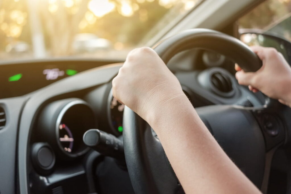 A closeup shot of two hands on the wheel as a person drives without their license.