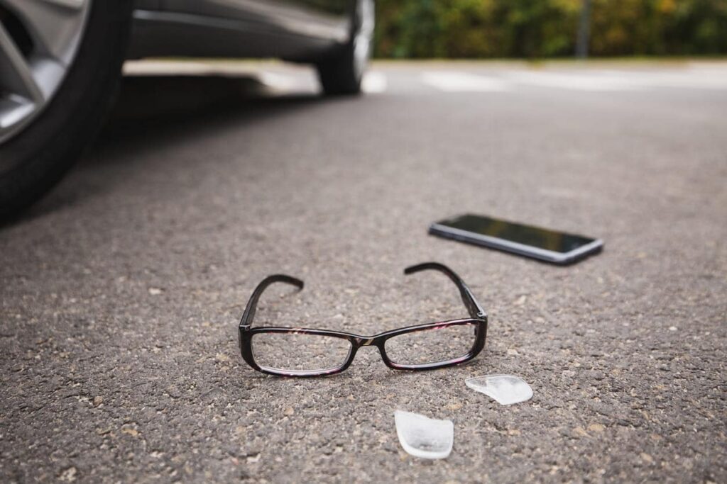 Broken glasses and a smartphone on the pavement after a pedestrian was hit by a car.