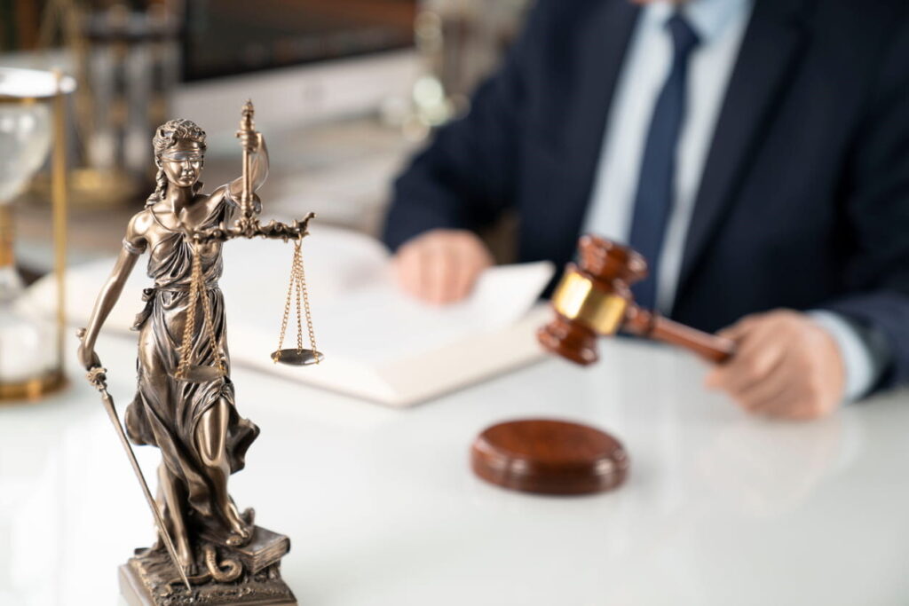 A wrongful death lawyer striking his gavel in the background at his desk. In the forefront is the Lady Justice statue.