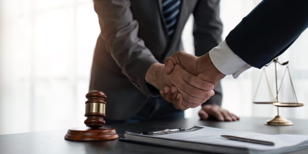 A truck accident attorney in Colorado shaking hands with their client. On the desk is paperwork, the scales of justice, and a gavel.