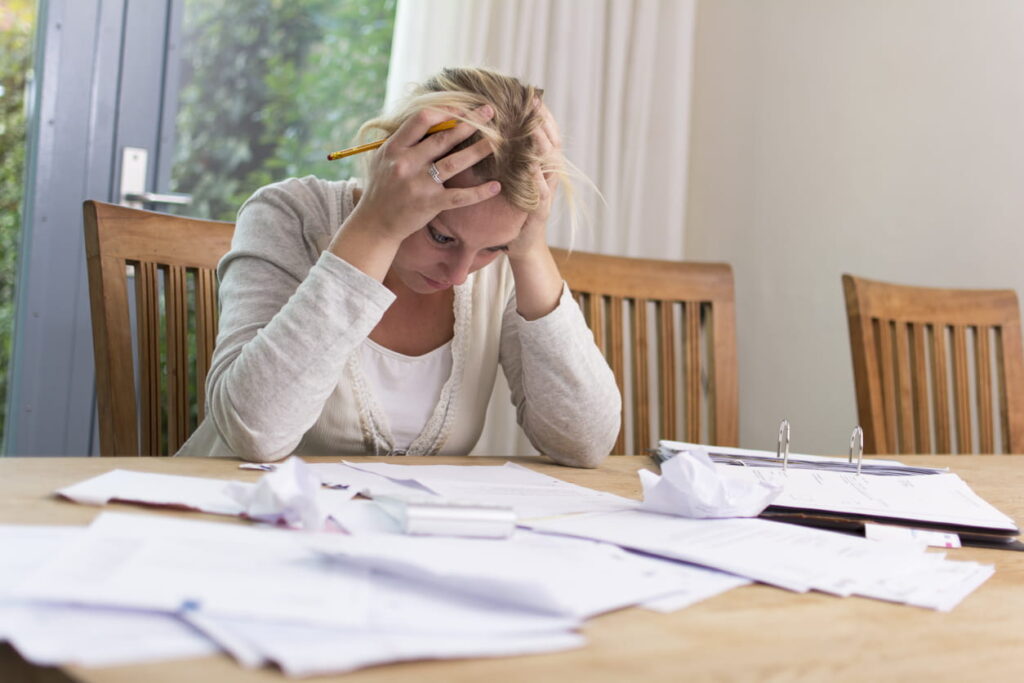 A woman in distress, holding her head while looking at medical bills after a personal injury.