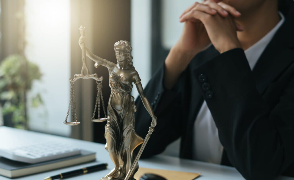 A wrongful death lawyer at his desk with his hands clasped. In front of him is a Lady Justice statue.