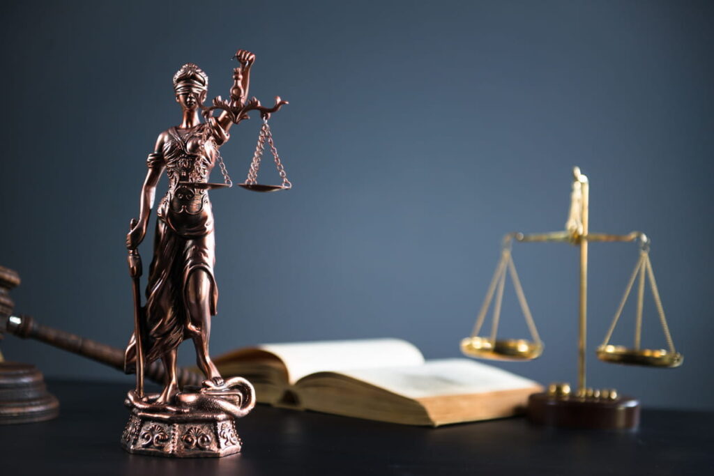 An open book, the scales of justice, a gavel, and a Lady Justice statue on a catastrophic injury attorney's desk.
