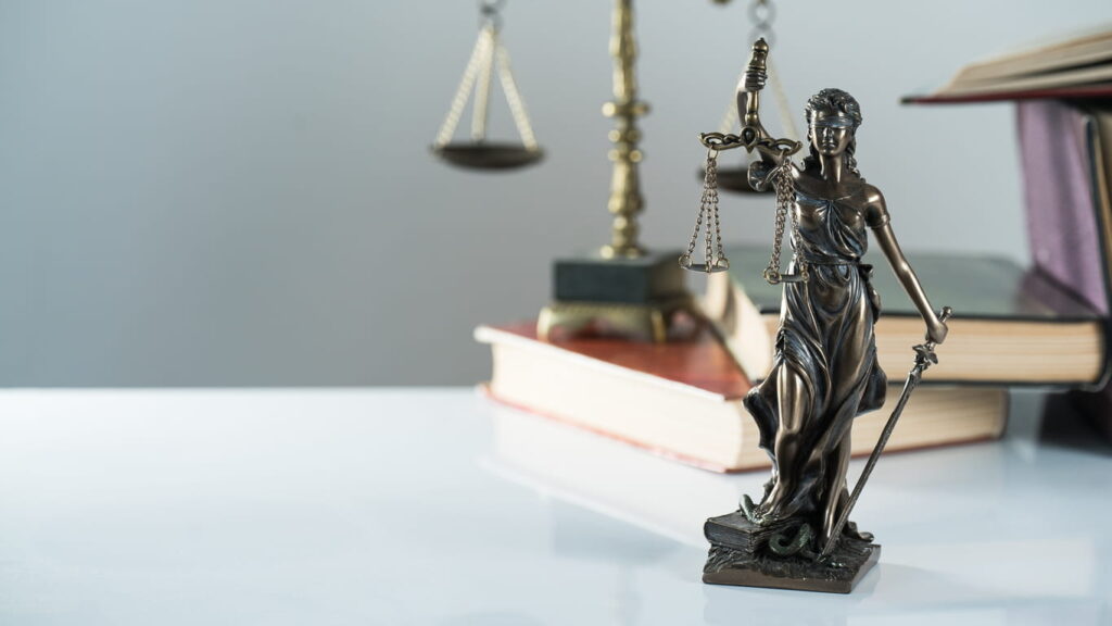 A Lady Justice statue in front of a stack of books and the scales of justice on a Colorado car accident attorney's desk.