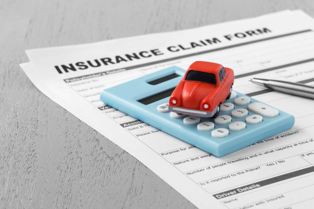 A red toy car, over a blue calculator that lies on top of an insurance claim form with a pen. 