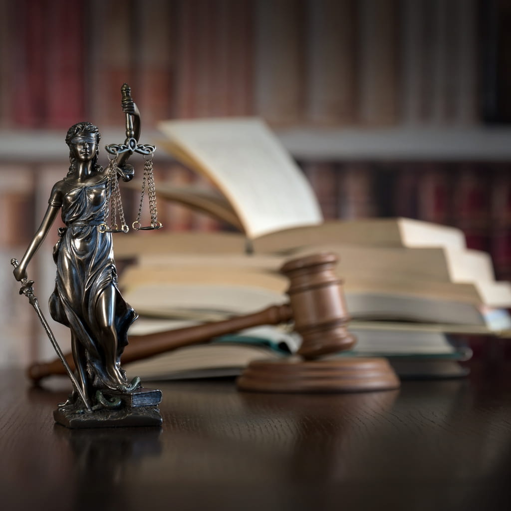 A Lady Justice statue on a Fort Collins employment law lawyer's desk, with a gavel and stack of books blurred out in the background. 