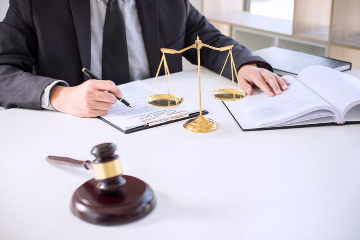 A personal injury lawyer working on a contract at his desk. Next to him is an open book, the scales of justice, and a gavel. 