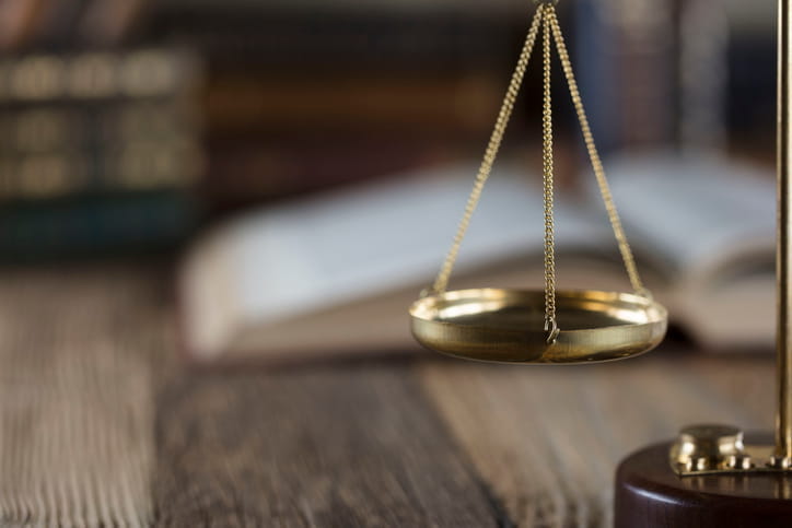 Focus is on one side of the scales of justice with a book blurred out in the background on a personal injury lawyer's desk. 