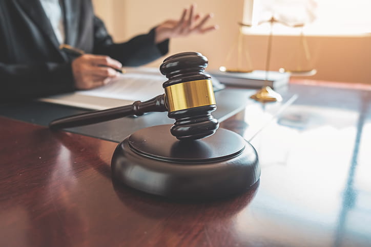A Colorado motorcycle injury attorney working on paperwork at his desk while speaking to someone off camera. The focus is on the gavel on his desk. In the background is the scales of justice.