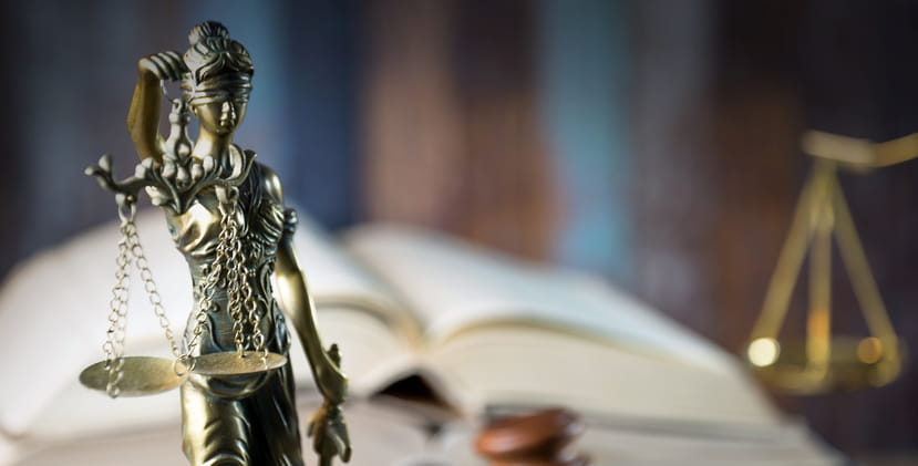 A closeup of a Lady Justice statue with a blurred out book and scales of justice in the background on a personal injury attorney's desk.