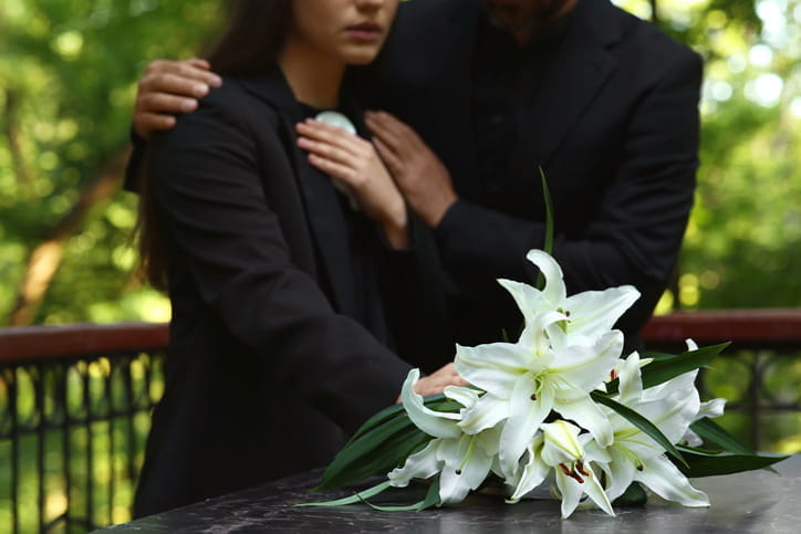 Two people grieving as they set flowers on top of a casket of their loved one.