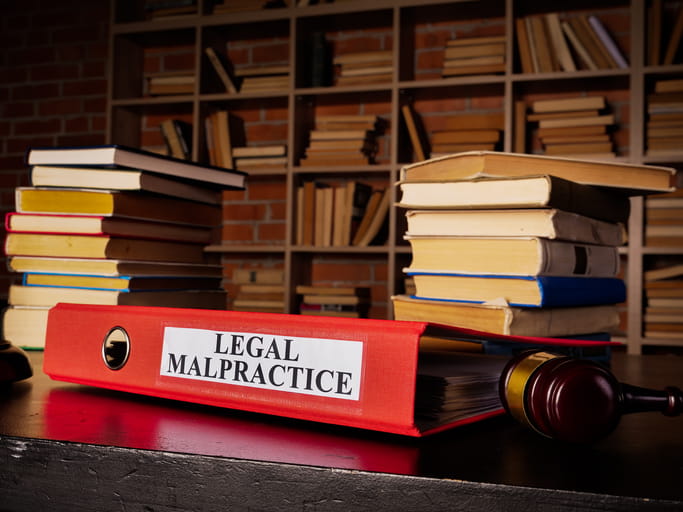 A red binder that reads: "Legal Malpractice." Next to it are stacks of books and a gavel. 