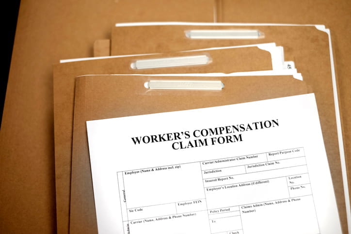 A form that reads: "Worker's Compensation Claim Form" on top a stack of brown folders.