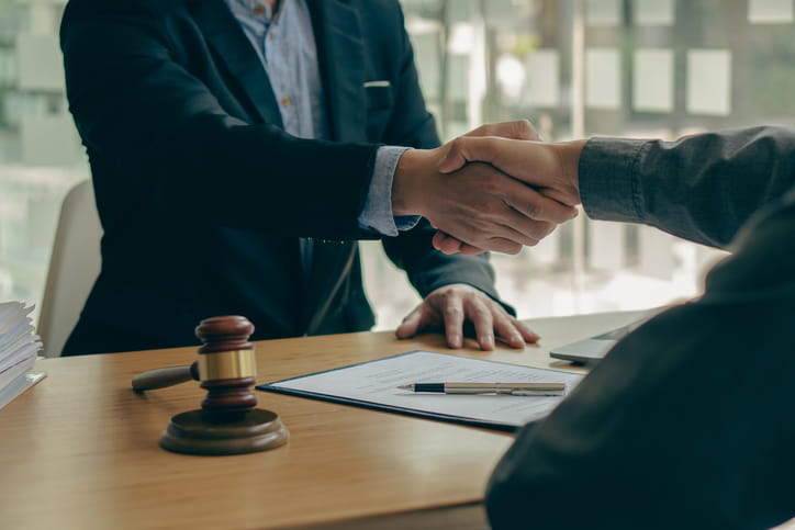 A personal injury attorney shaking hands with their client. On their desk is a gavel and paperwork. 