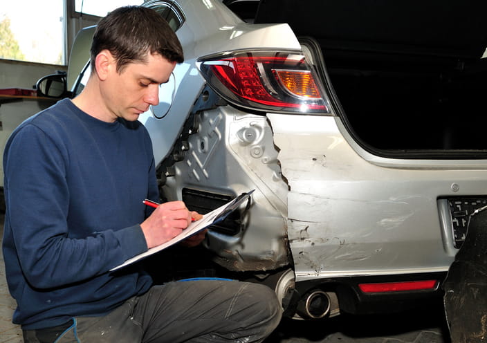 A man reporting on the damage to a vehicle after an accident to gather records to reconstruct the accident.