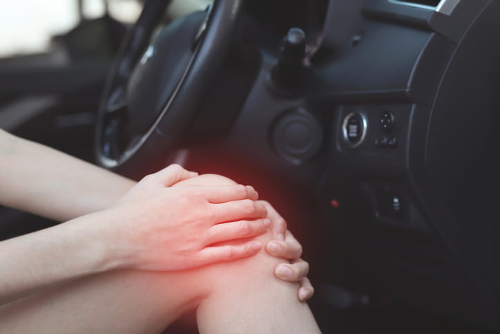 A person holding their knee in pain while sitting inside a vehicle after they've been in a car accident.