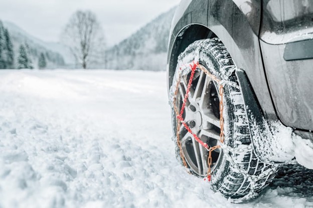 Chains on tires as a vehicle drives through snow.