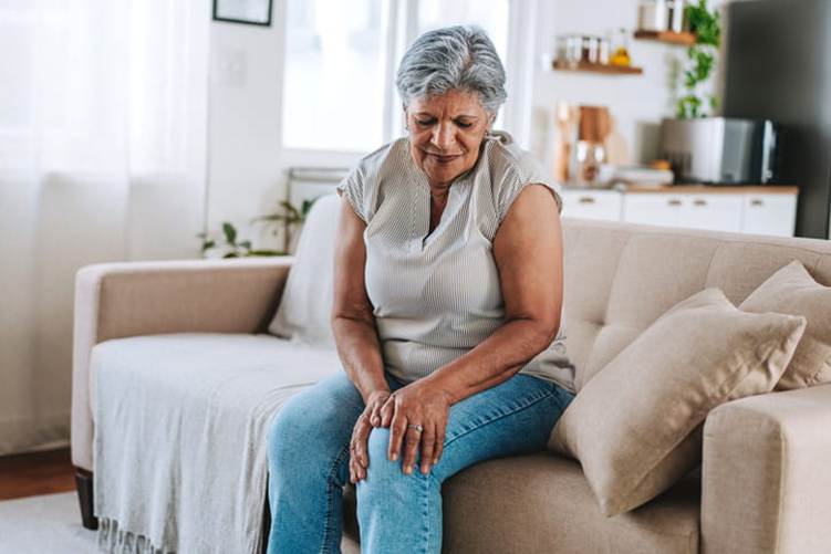 An elderly woman holds her leg in pain.
