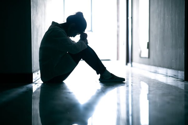 A silhouette of a woman sitting in a hallway with her head down.