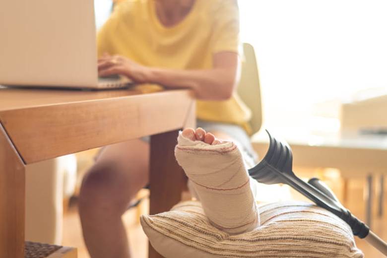 A woman with a broken leg sits at her table while working on a laptop.
