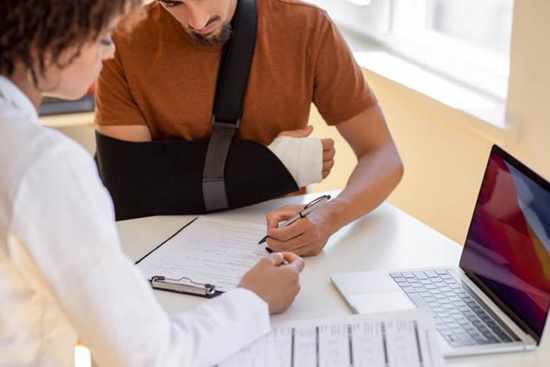 A person in a sling fills out paperwork with their personal injury lawyer.