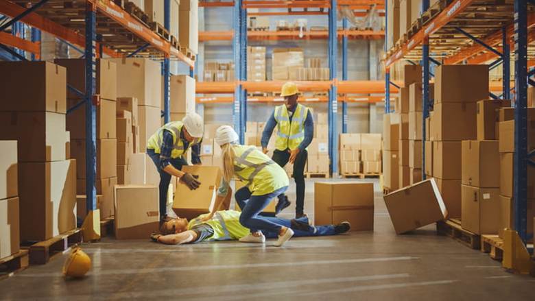Three workers help a coworker who is on the ground hurt after a warehouse accident.